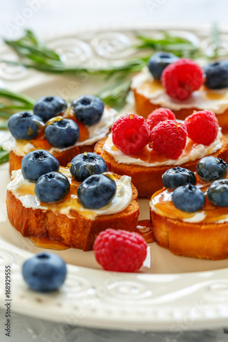 Slices of toasted bread with soft cheese and berries.