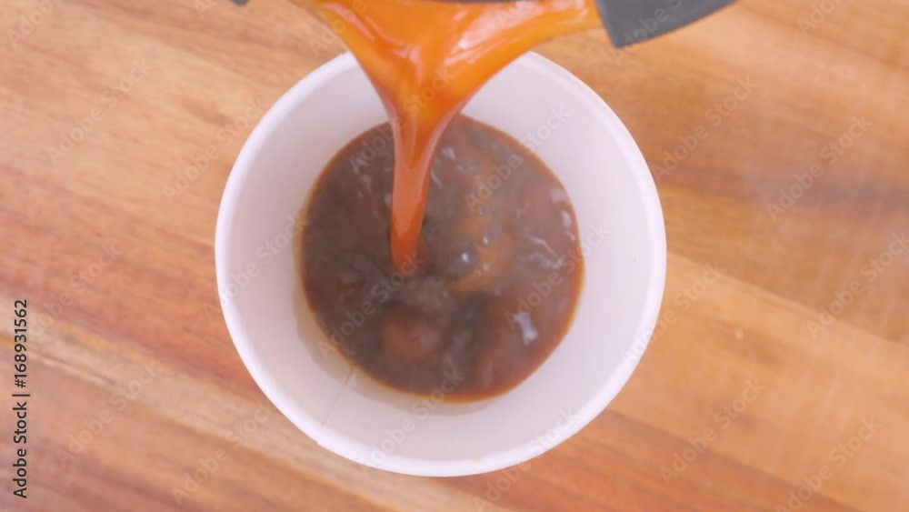 Coffee and milk pouring into paper cup on wooden background, hand takes cup away, slow motion