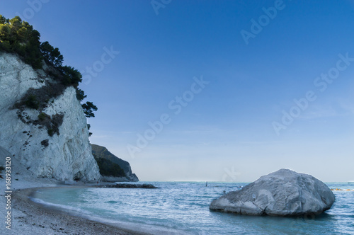 Fototapeta Naklejka Na Ścianę i Meble -  Sunset at the friars' beach ( spiaggia dei Frati ), Numana, Sirolo, Italy. A big rock in the sea near the shore on the right and the Conero's mount on the left. background like a postcard