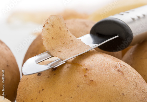 Potatoes, with a vegetable peeler on a white background, close up photo