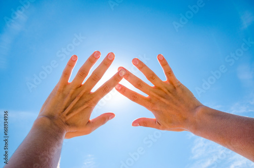 Two palms cover from the sun. First-person view of the sky. Sun is shining through fingers