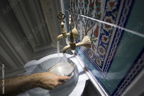 Detail of the hand filling the bath bowl from the faucet in the Turkish bath