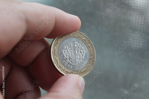 A coin worth 1 Turkish lira between the fingers of the hand.