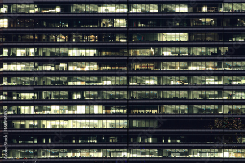 Multi-stories office building at night with worker working overtime. late night at office.  lighting and working people within. Late night overtime in a modern office building