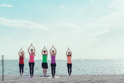 Young group man and woman yoga practice on mat relaxation in class exercise with pose fitness sport for healthy on the beach and seaside  modern city at sunrise relax,copy space the right.