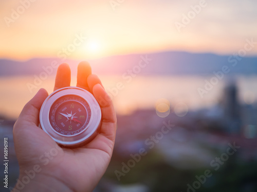 Closeup hand holding compass with  mountain and sunset sky background. photo