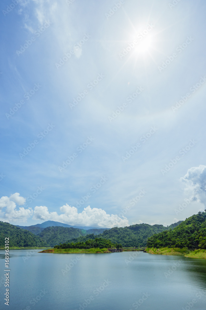 Lake with Mountains.Relax summer wallpaper, daytime landscape with lake among the wooded green mountains, beautiful blue cloudy sky and fantastic beautiful sun halo phenomenon in Thailand.