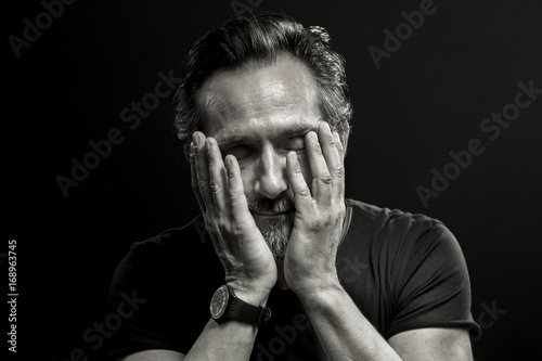 Monochrome portrait of mature man in crisis. Male covering his face with hands showing emotions of sorrow and regret.