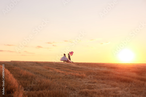 Bride and groom in a field at sunset with balloon