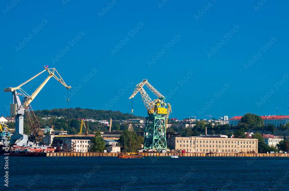Industrial cranes in the bay of the sea city on the background of houses.