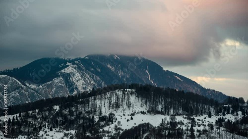 Sunset view of Postavaru Mountains from Paraul Rece in winter.	 Panoramic view with dramatic sky at sunset over Postavaru Mountains, Romania. 4k timelapse.  photo