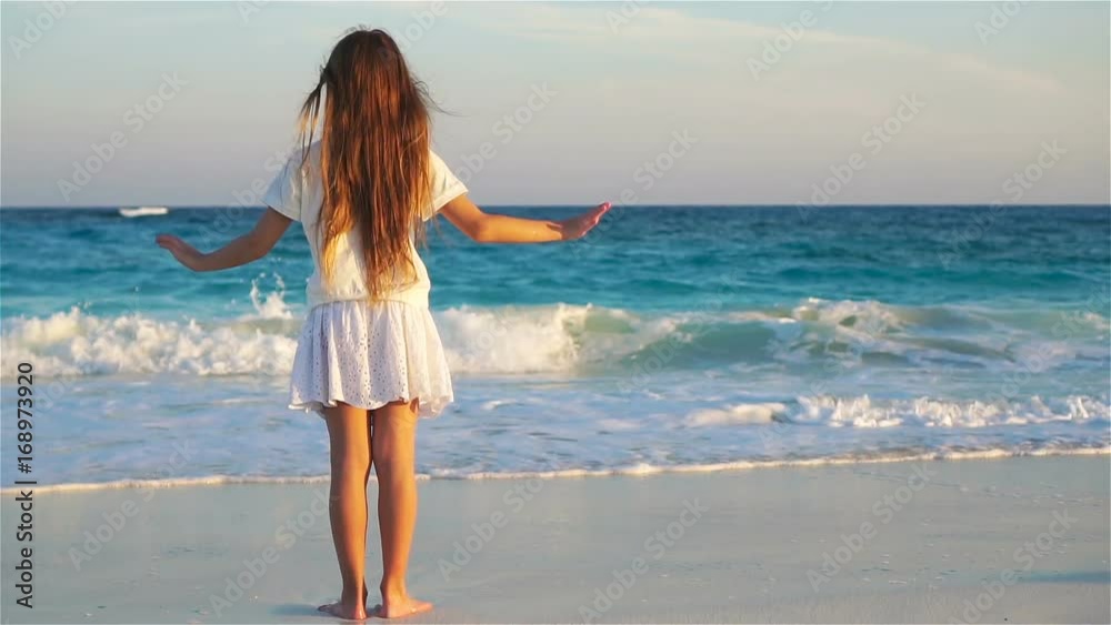 Adorable happy little girl on white beach looking on the ocean. Noisy sea and a small cute kid Adorable happy little girl on white beach looking on the ocean. Noisy sea and a small cute kid