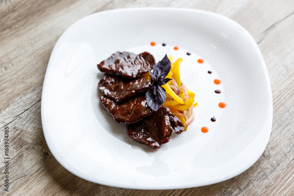 A white plate with slices of beef, stewed yellow pepper and onion. Purple basil on top. Drops of sauce. A white plate with slices of beef, stewed yellow pepper and onion. Purple basil on top. Drops of sauce.