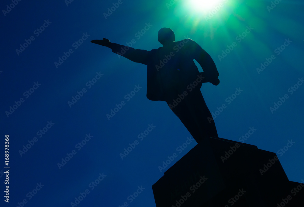 Lenin monument silhouette against blue sky with sun rays