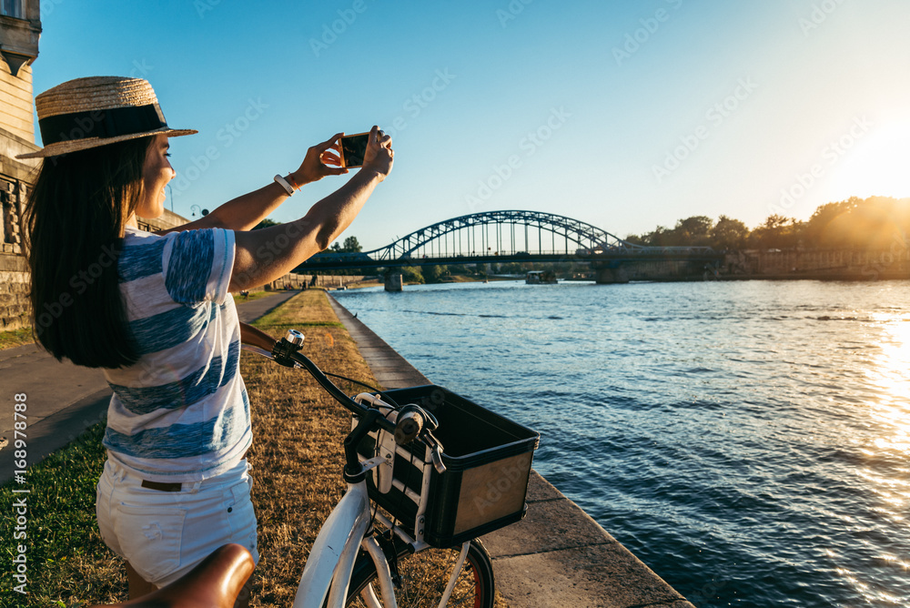 woman taking picture of the river at embankment on sunset