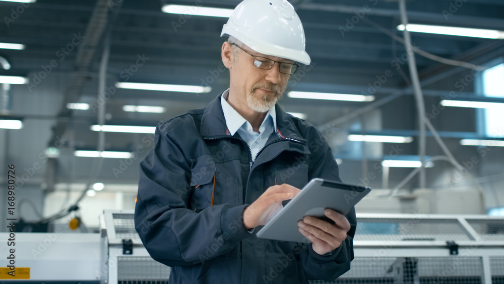 Senior engineer in hardhat is using a tablet computer in a factory. Senior engineer in hardhat is using a tablet computer in a factory.