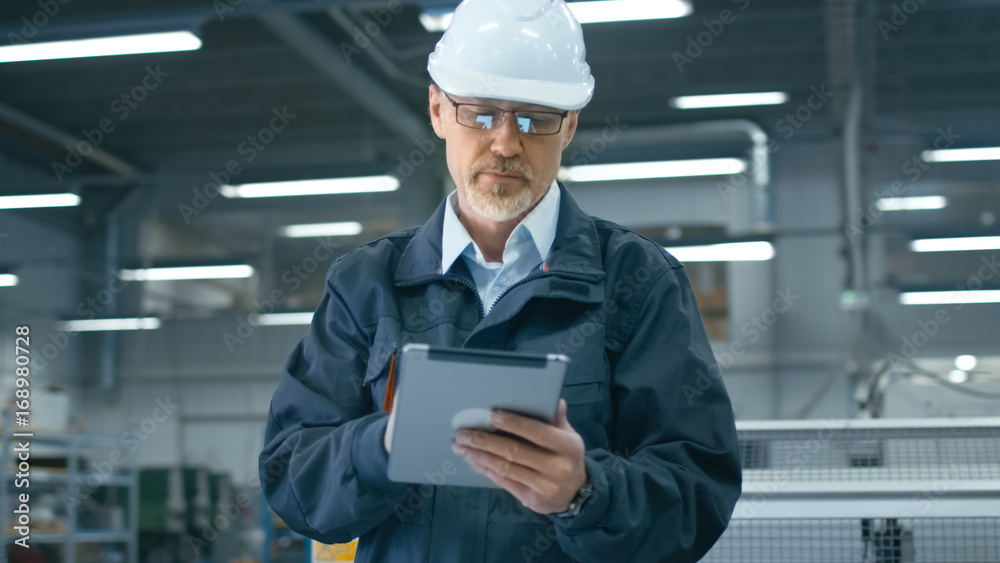 Senior engineer in hardhat is using a tablet computer in a factory. Senior engineer in hardhat is using a tablet computer in a factory.