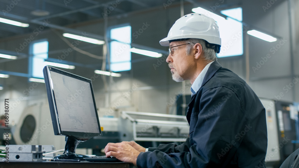 Senior engineer in glasses is working on a desktop computer in a factory. Senior engineer in glasses is working on a desktop computer in a factory.