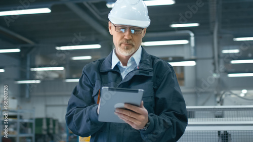 Senior engineer in hardhat is using a tablet computer in a factory.
