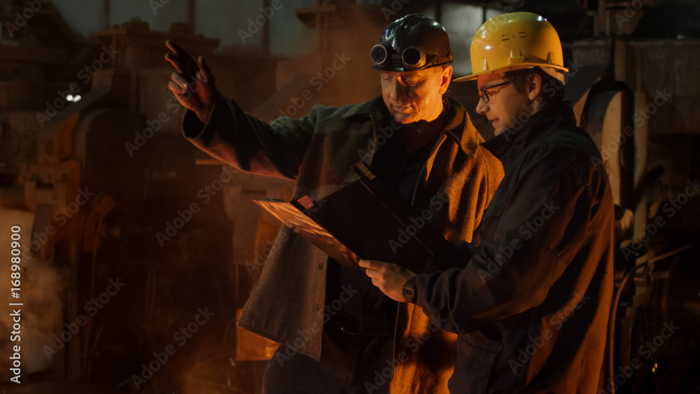 Engineer and Worker Have Conversation in Foundry. Engineer Using Tablet. Rough Industrial Environment.