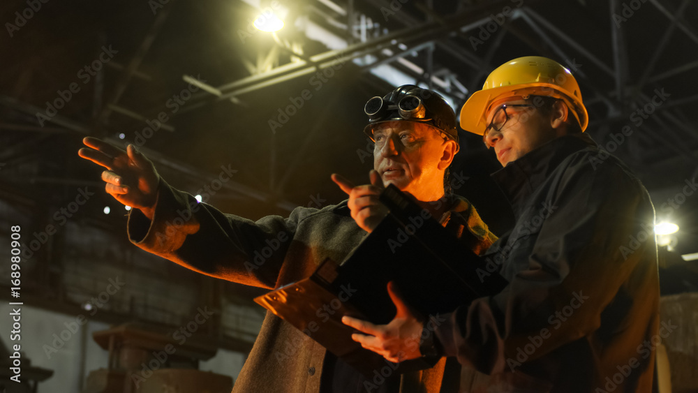 Fototapeta premium Engineer and Worker Have Conversation in Foundry. Engineer Using Tablet. Rough Industrial Environment.