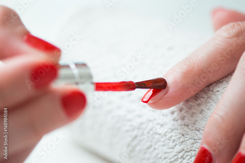 Obraz na plátně Closeup of a woman painting her nails with red nail polish