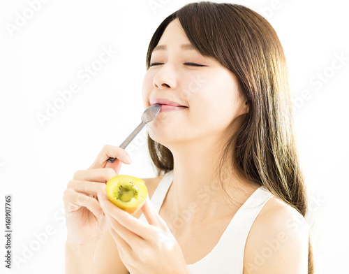 Happy young woman eating kiwi fruit