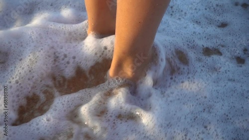 Closeup of child legs standing at the surf with flowing water