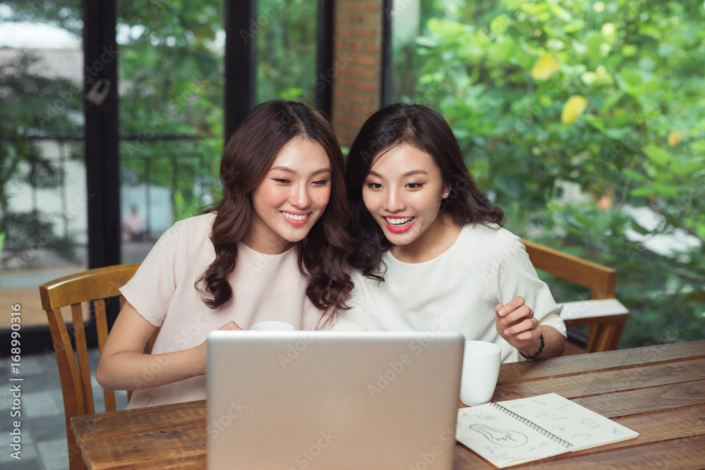 Two businesswomen working together. Girl is sitting at table in front of laptop Two businesswomen working together. Girl is sitting at table in front of laptop