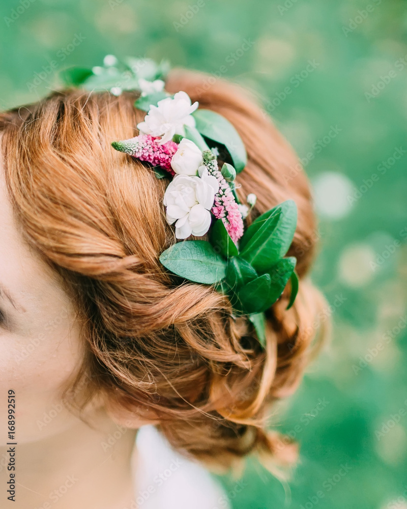 Naklejka premium Back view of unrecognizable young woman with red hair and wreath with flowers over blurred green background. Artwork