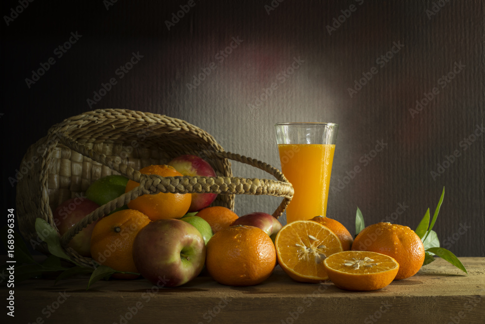 Many kinds of fruits in a in wicker basket  and orange juice on a wooden table, still life style.