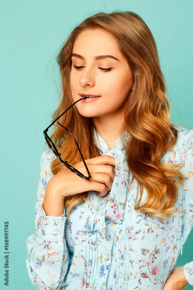 Pretty thoughtful girl with glasses in her mouth over blue background Pretty thoughtful girl with glasses in her mouth over blue background