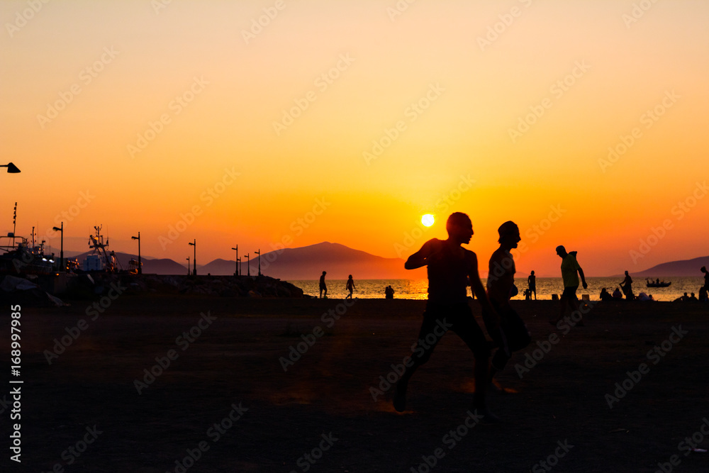 Silhouetted shot of young people are having fun on beach and playing football