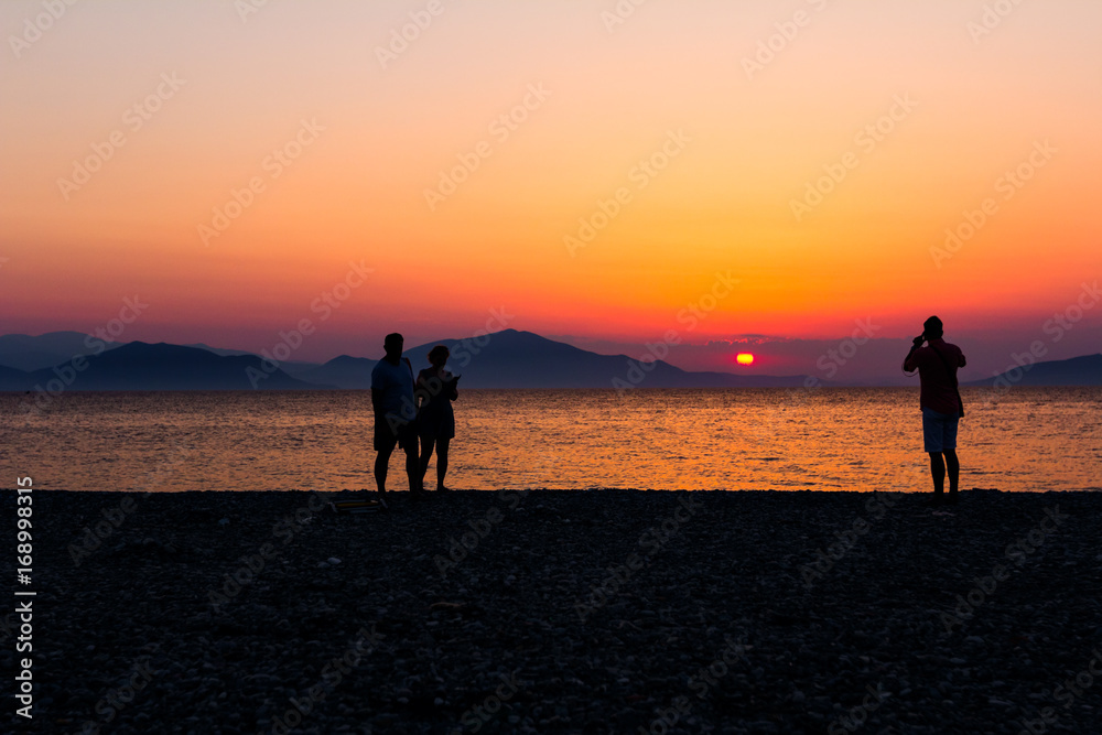 Silhouetted shot of sunset with couple, people by the beach