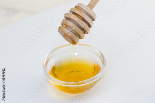 Honey dipper transferring honey and dripping into small glass bowl.Selective focus on the dipper