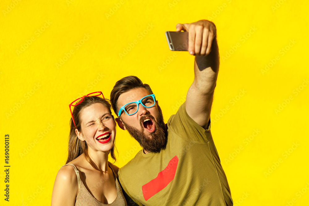 Fotografie Hipsters couple macking selfie on yellow background