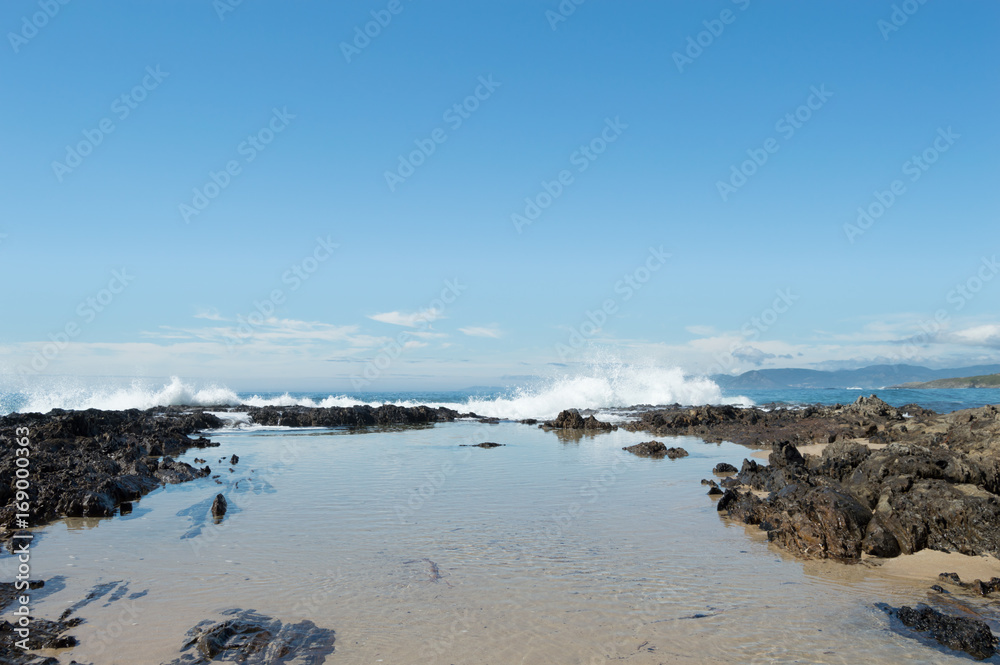Water in calm at the coast, with waves hitting the rocks behind Water in calm at the coast, with waves hitting the rocks behind