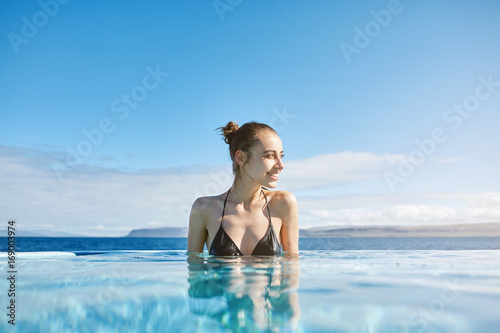 Young cheerful girl swimming in water of pool looking away on background of sea, Iceland, West Fjords. back view