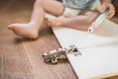 Baby holds a screwdriver and repairs furniture