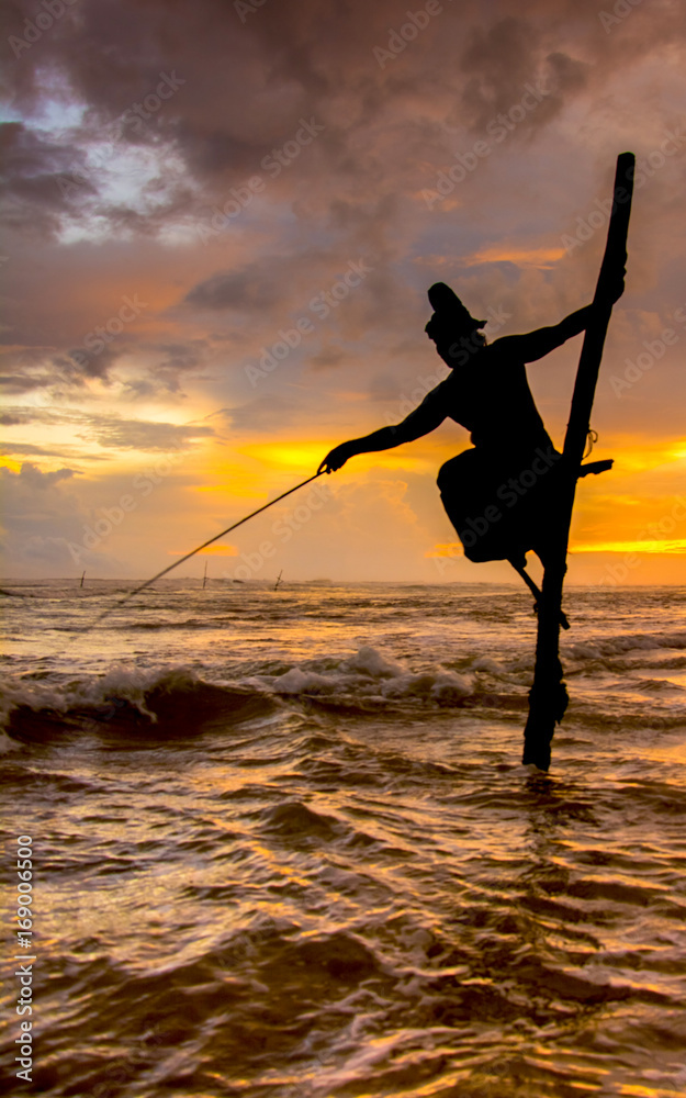 Silhouettes of the traditional Sri Lankan stilt fishermen at the sunset in  Weligama, Sri Lanka. Stilt fishing is a method of fishing unique to the  island country of Sri Lanka Stock Photo