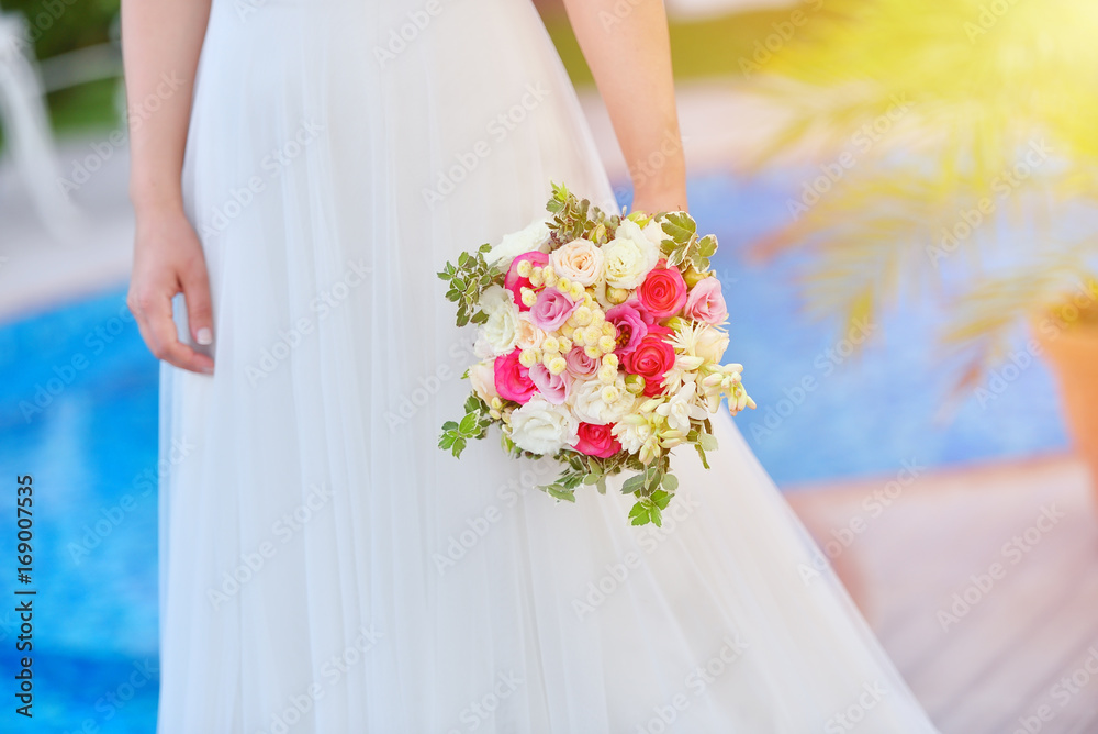 Bride in wedding dress holds her rouses bouquet against blue pool Bride in wedding dress holds her rouses bouquet against blue pool