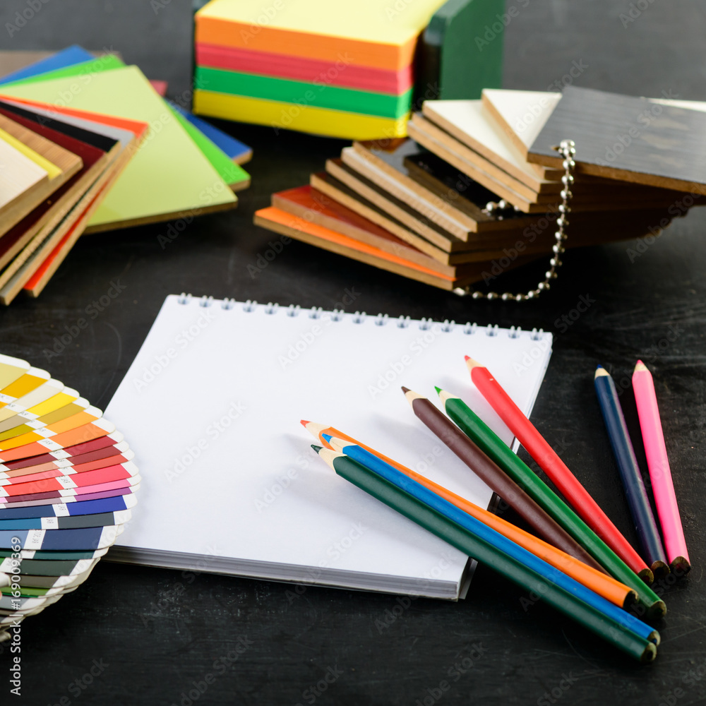 Fototapeta premium creative professional modern designer workplace in the office. Close-up open notebook, pens, stickers, material samples and color charts, concept of choosing color of interior