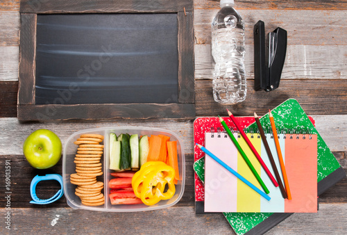 School supplies and lunch on wooden background.
