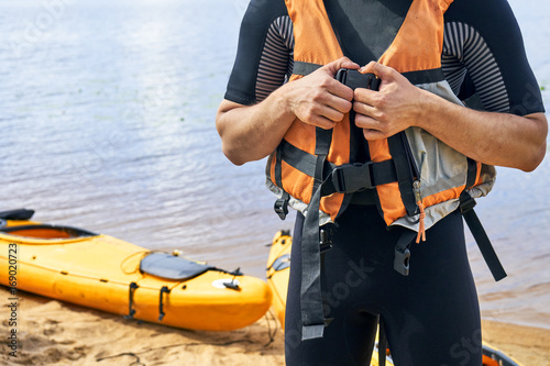  Young hiker wearing wetsuit putting on a life jacket before sailing on kayak 