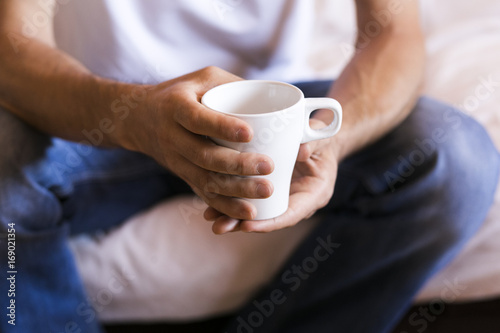 man hands holding a white cup of coffee in the morning. Sitting on the sofa. Daytime. Lifestyle