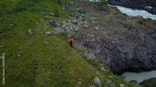 Aerial. girl traveler with backpack walks along the cliff in the mountains. woman tourist went Hiking. Altai, Siberia. Aerial camera shot