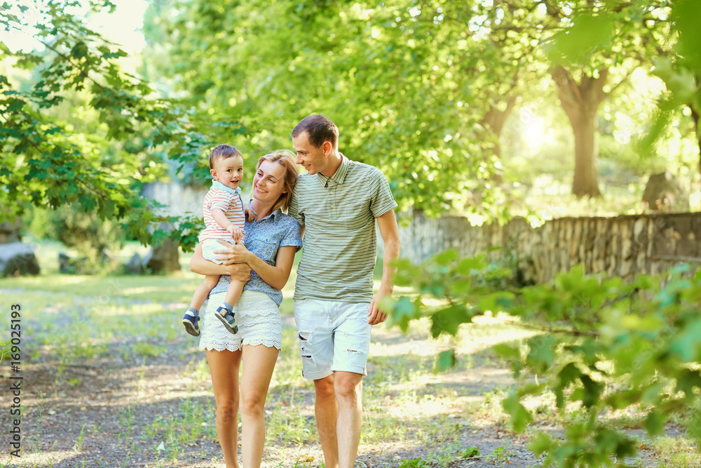 Fototapeta premium Happy young family walking in summer park. Mother father and little child son play in nature.