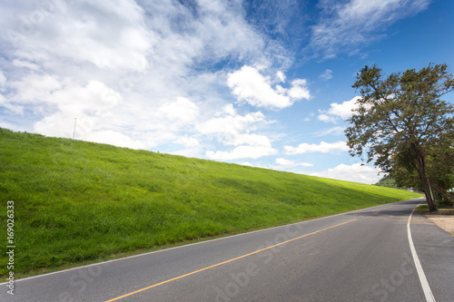 Road with green grass field under white clouds and blue sky. © Jirapas