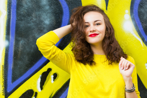 Portrait of cute girl in yellow pullover on graffiti wall background © dtatiana