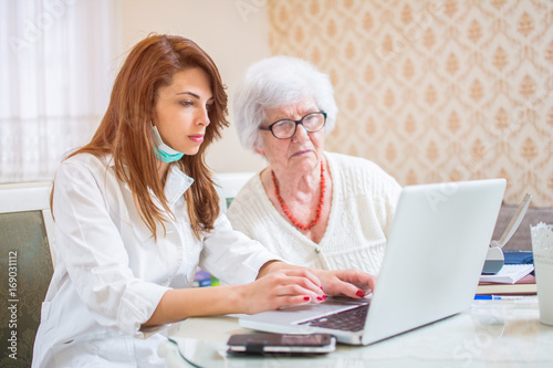 Nurse and senior woman looking together at medical record on laptop.